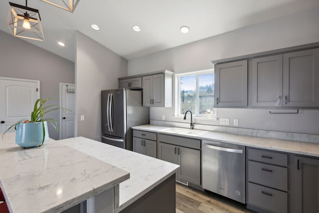 kitchen featuring sink, appliances with stainless steel finishes, gray cabinets, a kitchen island, and light stone countertops