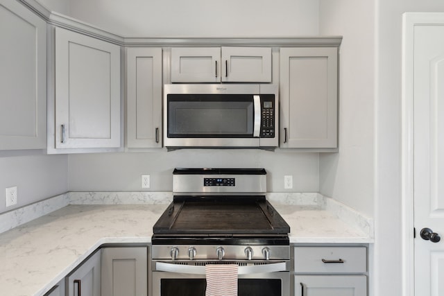 kitchen with gray cabinetry, light stone countertops, and appliances with stainless steel finishes