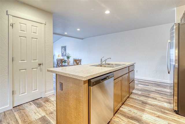 kitchen featuring a kitchen island with sink, sink, stainless steel appliances, and light wood-type flooring