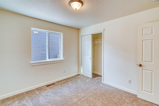 unfurnished bedroom featuring light carpet, a closet, and a textured ceiling