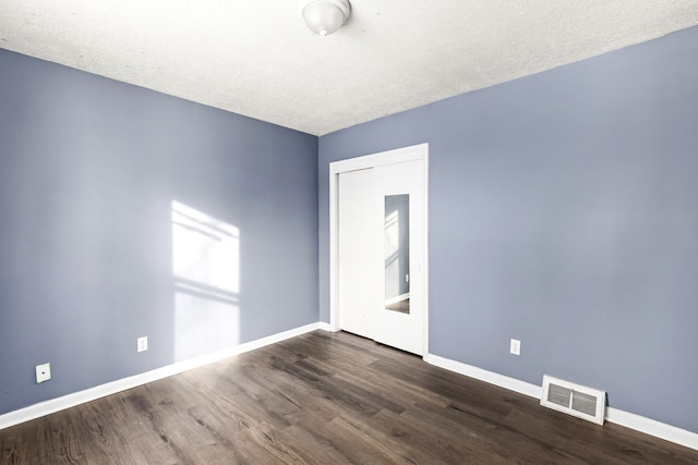 empty room with dark hardwood / wood-style floors and a textured ceiling