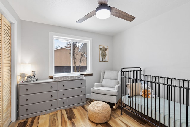 bedroom with a crib, light hardwood / wood-style floors, a closet, and ceiling fan