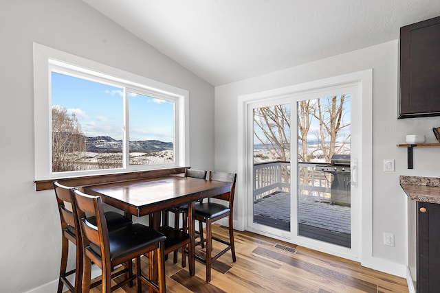 dining space featuring a mountain view, vaulted ceiling, and light wood-type flooring