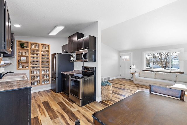 kitchen with vaulted ceiling, sink, stainless steel appliances, a textured ceiling, and light hardwood / wood-style flooring