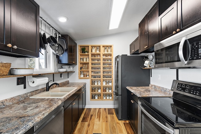 kitchen featuring appliances with stainless steel finishes, lofted ceiling, sink, dark stone counters, and light wood-type flooring