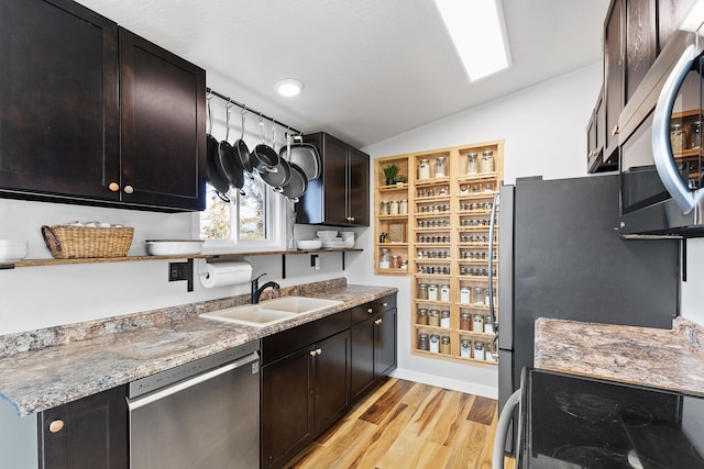 kitchen with sink, vaulted ceiling, light wood-type flooring, appliances with stainless steel finishes, and light stone countertops