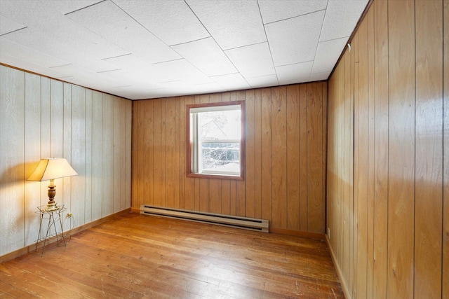 empty room with wood walls, baseboard heating, and light hardwood / wood-style floors