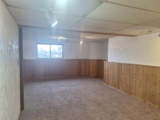 carpeted spare room featuring wainscoting, a paneled ceiling, and wooden walls