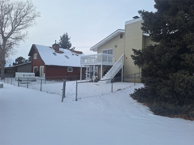 snow covered house with stairway, fence, a chimney, and a wooden deck