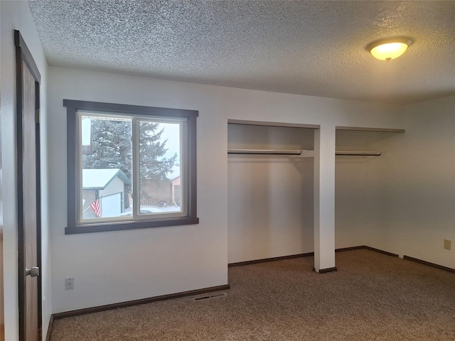 unfurnished bedroom with carpet flooring, a textured ceiling, baseboards, and two closets