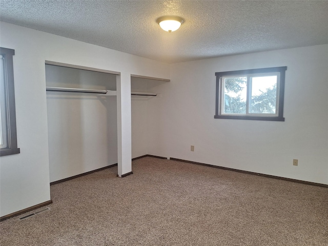 unfurnished bedroom featuring a textured ceiling, carpet floors, visible vents, baseboards, and multiple closets