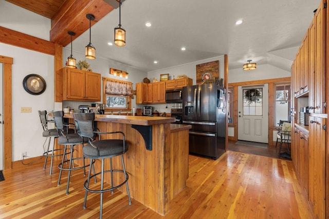 kitchen with hanging light fixtures, light wood-type flooring, a kitchen breakfast bar, and black fridge