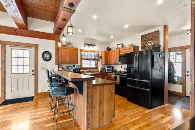 kitchen featuring electric range oven, a wealth of natural light, hanging light fixtures, beam ceiling, and black refrigerator with ice dispenser