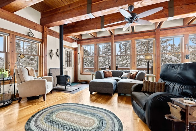 sunroom featuring beamed ceiling, ceiling fan, a wealth of natural light, and a wood stove