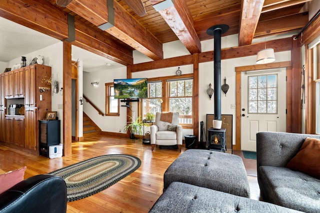 living room featuring beamed ceiling, a wealth of natural light, light hardwood / wood-style flooring, and a wood stove