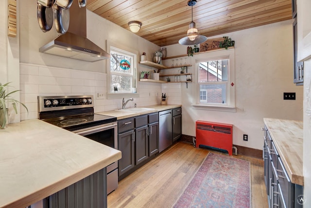 kitchen featuring wall chimney range hood, sink, butcher block counters, hanging light fixtures, and stainless steel appliances