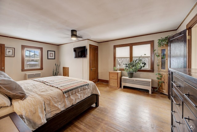 bedroom featuring light hardwood / wood-style flooring, a wall mounted air conditioner, radiator heating unit, and ornamental molding