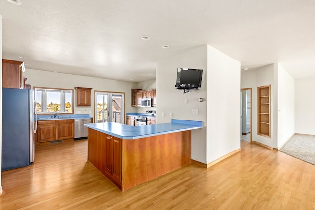 kitchen featuring a peninsula, appliances with stainless steel finishes, brown cabinetry, and light wood-style floors