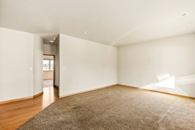 empty room featuring a textured ceiling, light wood-style floors, light colored carpet, and baseboards