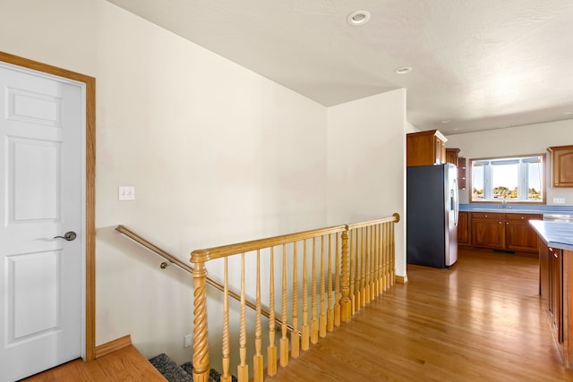 hallway with light wood-type flooring, a sink, and an upstairs landing