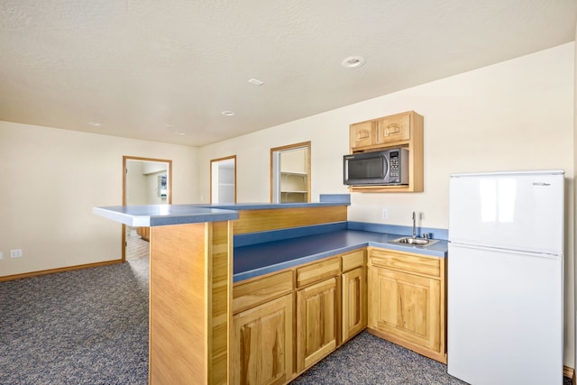 kitchen with a breakfast bar area, dark colored carpet, freestanding refrigerator, a sink, and a peninsula