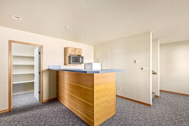 kitchen featuring stainless steel microwave, dark carpet, a peninsula, and a textured ceiling