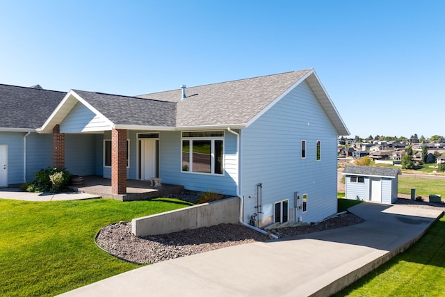 single story home featuring covered porch, a front lawn, a shingled roof, and an outdoor structure