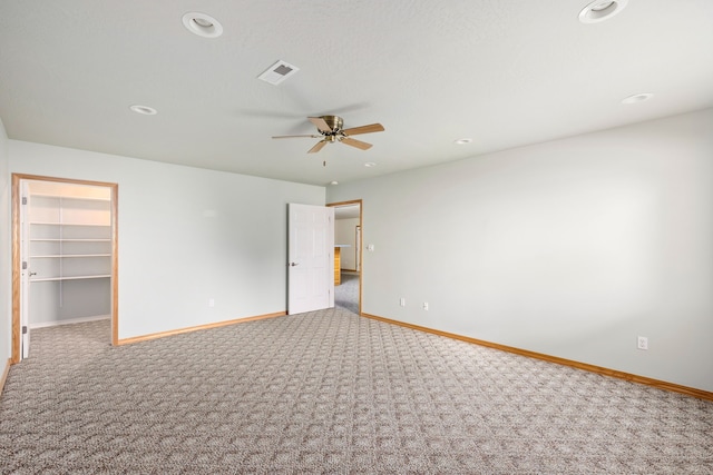 unfurnished bedroom with carpet floors, visible vents, a spacious closet, a ceiling fan, and baseboards