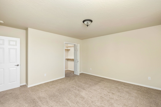 unfurnished bedroom with a textured ceiling, light carpet, baseboards, a spacious closet, and a closet