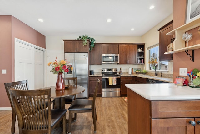 kitchen featuring sink, stainless steel appliances, kitchen peninsula, and light wood-type flooring