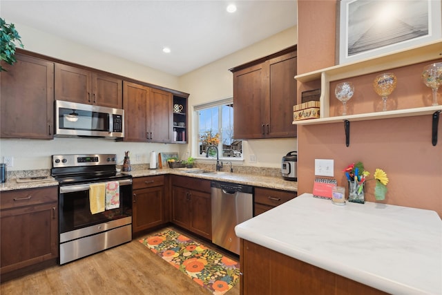 kitchen with sink, dark brown cabinets, light hardwood / wood-style flooring, appliances with stainless steel finishes, and light stone countertops