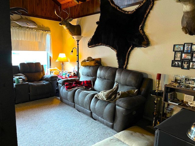 living room with vaulted ceiling with beams, light colored carpet, and wood ceiling