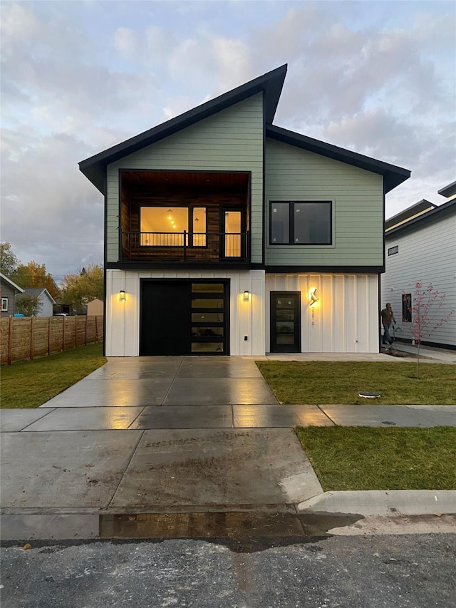 contemporary home featuring driveway, fence, board and batten siding, a front yard, and a balcony