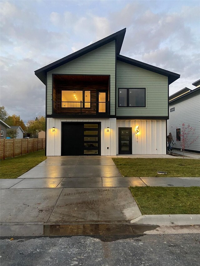 contemporary home with driveway, a balcony, fence, board and batten siding, and a front yard