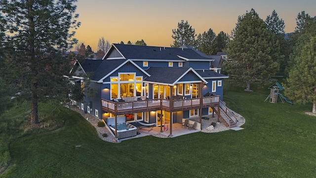 back house at dusk with a deck, a patio area, and a lawn