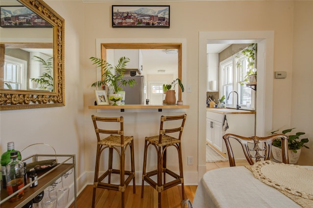 bar with light wood-type flooring, a wealth of natural light, baseboards, and a sink