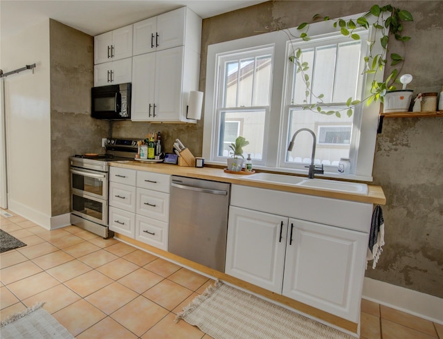 kitchen with a sink, white cabinetry, appliances with stainless steel finishes, and light tile patterned flooring