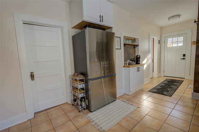 kitchen featuring baseboards, freestanding refrigerator, white cabinetry, and light tile patterned flooring