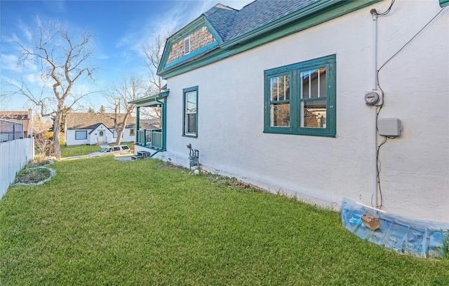 view of side of property featuring stucco siding, fence, roof with shingles, and a lawn