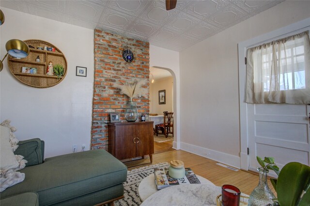 living area with light wood-style flooring, arched walkways, an ornate ceiling, baseboards, and visible vents
