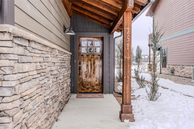 snow covered property entrance featuring stone siding