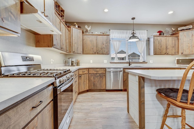 kitchen featuring a kitchen bar, sink, light wood-type flooring, appliances with stainless steel finishes, and pendant lighting