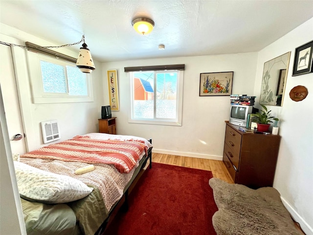 bedroom with multiple windows, hardwood / wood-style flooring, and heating unit