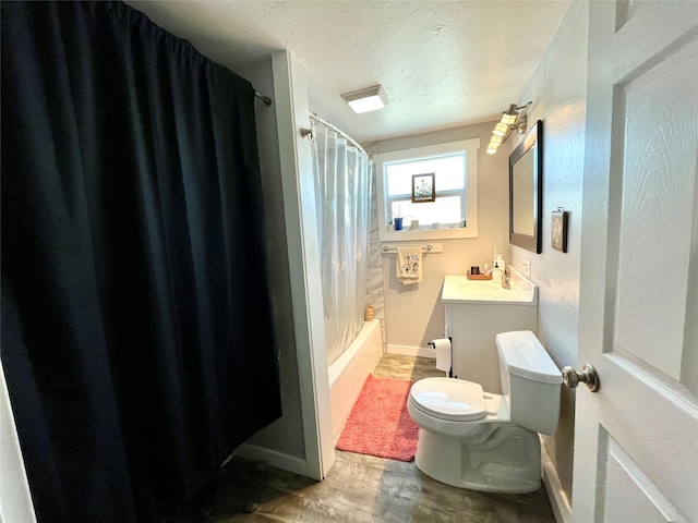 full bathroom with hardwood / wood-style floors, vanity, shower / tub combo, toilet, and a textured ceiling