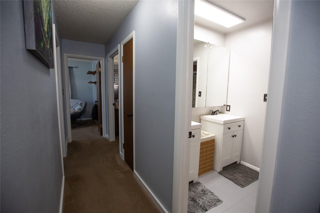 hallway with light carpet, sink, and a textured ceiling