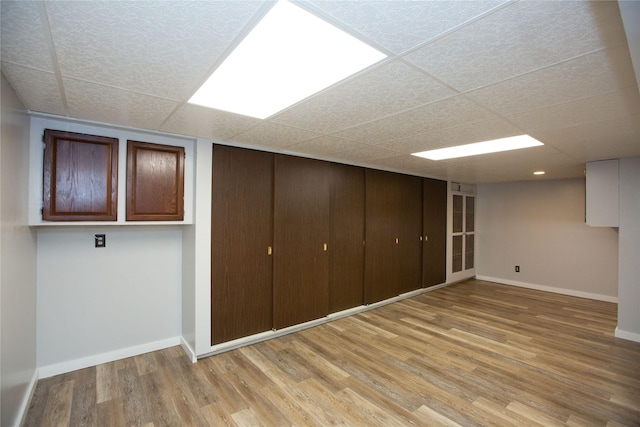 basement with light hardwood / wood-style flooring and a paneled ceiling