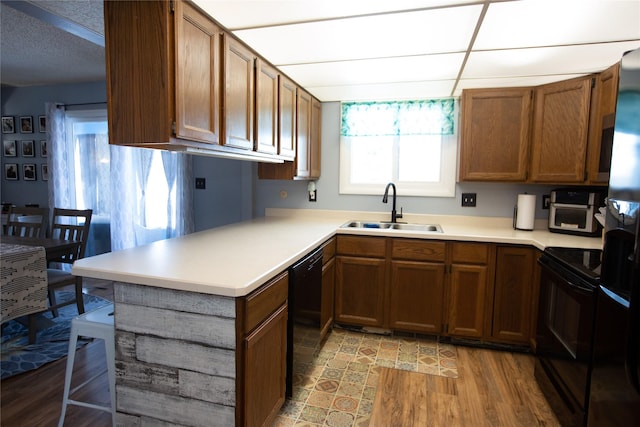 kitchen featuring kitchen peninsula, sink, light hardwood / wood-style flooring, and black appliances