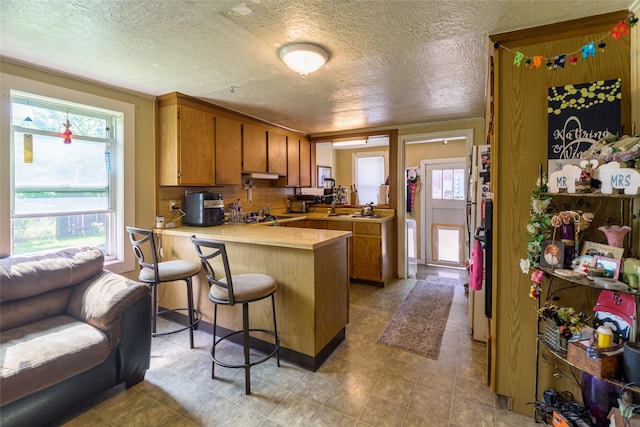 kitchen with a breakfast bar, sink, backsplash, kitchen peninsula, and a textured ceiling