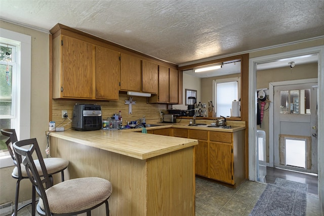 kitchen featuring a breakfast bar area, a baseboard radiator, kitchen peninsula, and a textured ceiling