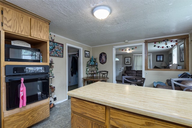 kitchen with dark tile patterned floors, crown molding, a textured ceiling, and black appliances